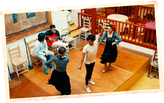Гитарист и певица беседуют, два танцора фламенко обучают человека шагам.